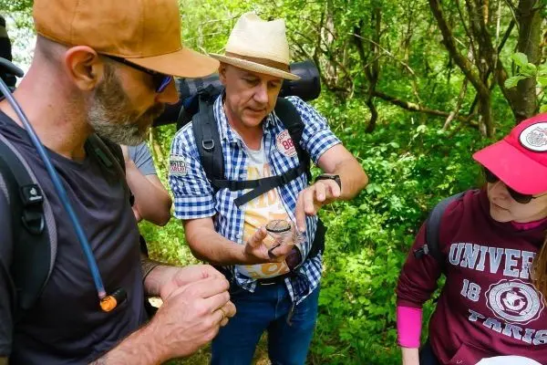 Mann zeigt Gruppe ein kleines Behältnis in der Natur